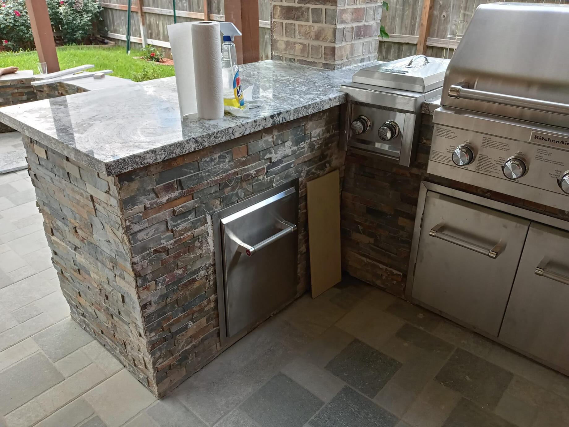 A nice stacked-stone outdoor kitchen area with grey marbled granite on top.